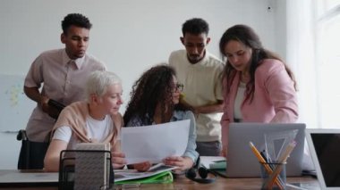 Genç çoklu etnik gruplar masada oturarak bir projeyi tartışıyorlar. Belgeler üzerinde çalışan meslektaşlar. Üretken takım çalışması. Ofiste ekip konuşuyor ve gülümsüyor. Yüksek kalite 4k görüntü