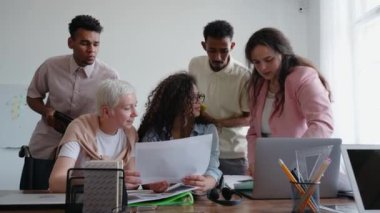 Genç çoklu etnik gruplar masada oturarak bir projeyi tartışıyorlar. Belgeler üzerinde çalışan meslektaşlar. Üretken takım çalışması. Ofiste ekip konuşuyor ve gülümsüyor. Yüksek kalite 4k görüntü