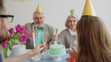 Mutlu yaşlı çiftler mutlu bir doğum günü partisinde aileleriyle kadeh tokuşturur. Pastel renkli parti, kafasında koni olan. Yaşlı bir çift kutlama yapıyor. Yüksek kalite 4k görüntü