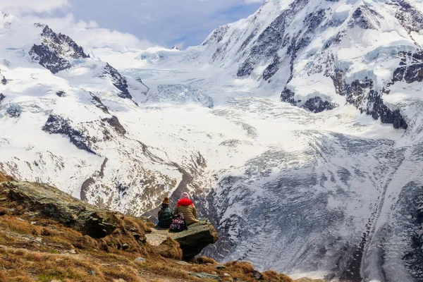 母と娘は石の上に座って 有名なゴーナー氷河と印象的な雪を持つペニーネアルプスのパノラマを見て スイスのツェルマットの近くにモンテ ローザ マッシフをキャップしました — ストック写真