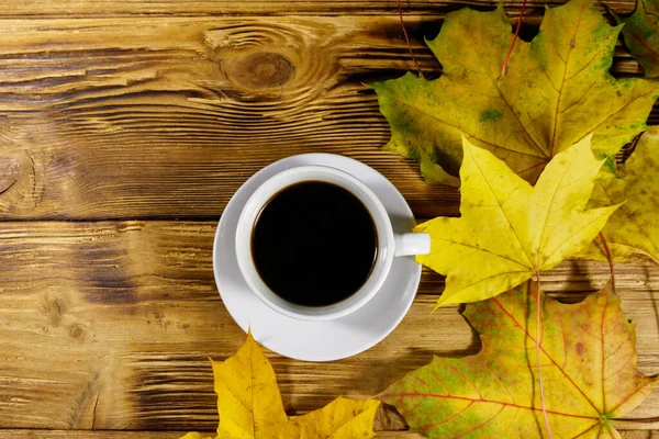 stock image Cup of coffee and autumn maple leaves on wooden table. Top view. Autumn concept