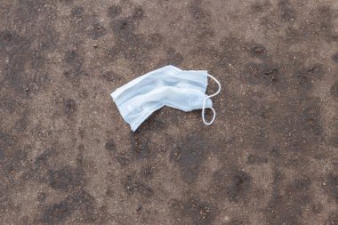 Kirli, tek kullanımlık tıbbi maske. Asfalt sokağa çöp olarak atılmış. COVID-19 sırasında israf. Koronavirüs salgınından kaynaklanan kirlilik