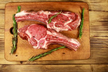 Kemiğin üzerinde çiğ biftek, baharatlar ve ahşap masada biberiye. Üst görünüm