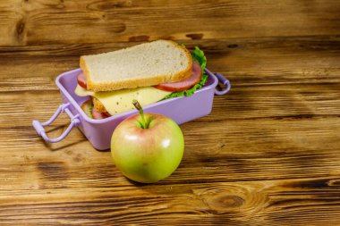 Tahta bir masada, sandviç ve elmayla beslenme çantası.