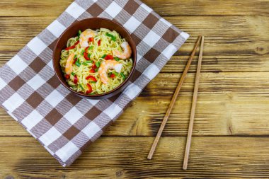 Bir kase karidesli Çin eriştesi, yeşil soğan ve ahşap masada kırmızı acı biber. Üst görünüm