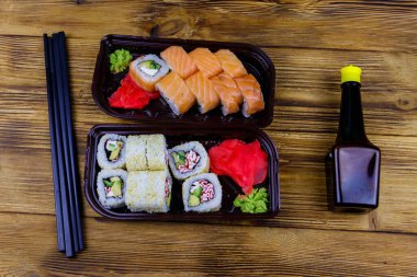 Plastik kutularda suşi ruloları, soya sosu ve ahşap masada yemek çubukları. Üst Manzara. Plastik kaplarda suşi servis etmek için suşi.