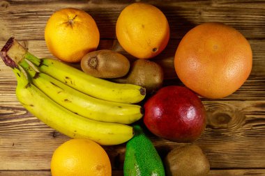 Ahşap masa üzerinde tropikal meyve çeşitleri. Muz, mango, portakal, avokado, greyfurt ve kivi ile natürmort. Üstte görüntü