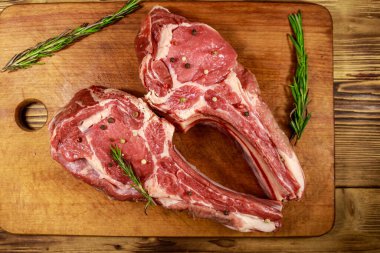 Kemiğin üzerinde çiğ biftek, baharatlar ve ahşap masada biberiye. Üst görünüm