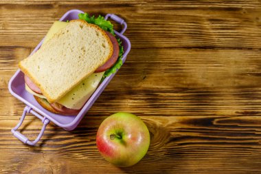 Tahta bir masanın üzerinde sandviç ve elma olan beslenme çantası. Üst görünüm, alanı kopyala