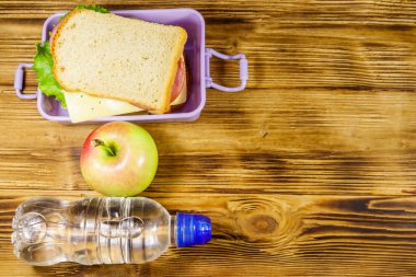 Sandviçli beslenme çantası, ahşap bir masada bir şişe su ve elma. Üst görünüm, alanı kopyala