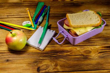 Okul konseptine geri dönelim. Okul gereçleri, elma ve beslenme çantası ve ahşap bir masada sandviçler.
