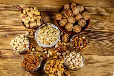 Ahşap masada fındık çeşitleri. Badem, fındık, fıstık, fıstık, ceviz ve küçük kaselerde kaju. Üst Manzara. Sağlıklı yeme kavramı