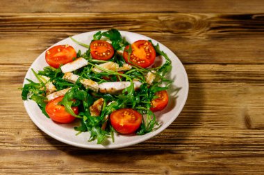 Lezzetli tavuk göğsü salatası, taze roka ve ahşap masada kiraz domatesleri.