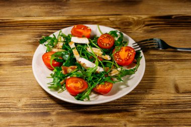 Lezzetli tavuk göğsü salatası, taze roka ve ahşap masada kiraz domatesleri.