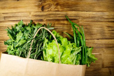 Yeşil soğanlı kağıt torbası, biberiye, marul yaprakları ve ahşap masada maydanoz. Üst Manzara. Sağlıklı gıda ve market alışverişi kavramı