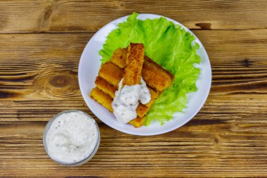 Tabakta kızarmış balık kroket, marul ve ahşap masada tartar sosu. Üst görünüm