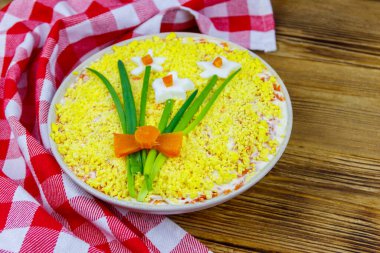 Geleneksel Rus katmanlı salata Mimosa, bahar süslemesi ahşap masa üzerinde Daffodil. Dekorasyon yumurta, yeşil soğan ve havuçtan yapılır.