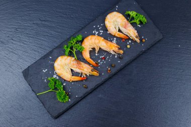 Siyah zemin üzerinde maydanozlu, tuzlu ve biberli büyük çiğ karidesler. Üst görünüm