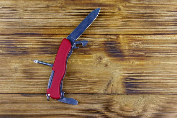 Red all purpose pocket knife on a rustic wooden background. Top view