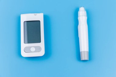 Pastel mavi arka planda dijital glukometre ve tükenmez kalem. Üst Manzara. Diyabet kavramı