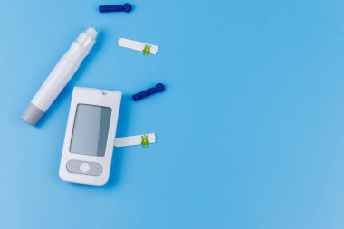 Dijital glukometre, tükenmez kalem, tek kullanımlık iğneler ve pastel mavi arka planda test şeritleri. Üst görünüm, boşluğu kopyala. Diyabet kavramı