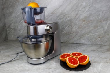 Mutfak masasında modern elektrik sıkacağı ve greyfurt. Taze sıkılmış greyfurt suyu hazırlanıyor.