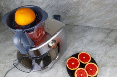 Mutfak masasında modern elektrik sıkacağı ve greyfurt. Taze sıkılmış greyfurt suyu hazırlanıyor.