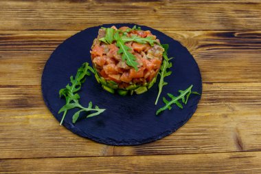Avokado ve roka ile ahşap masada somon tartar.
