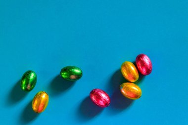 Mavi arka planda folyo içinde paskalya çikolatası yumurtaları. Üst görünüm