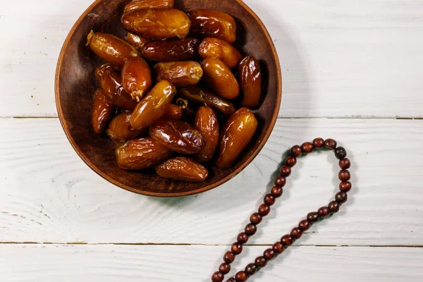 Dates fruit and rosary on white wooden table. Top view. The Muslim feast of the holy month of Ramadan