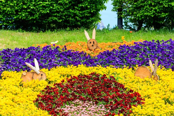 春の公園で木製のイースターバニーで飾られたパンジーやデイジーのカラフルな花壇 — ストック写真