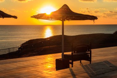 Güneşin doğuşunda deniz manzaralı plaj güneşinin altında rahat bir bank. Yaz tatilleri konsepti