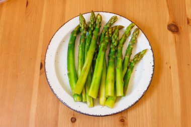 Ahşap bir masada yeşil haşlanmış kuşkonmaz.