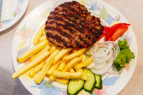 Grilled minced beef patty served with french fries and fresh vegetables on a table
