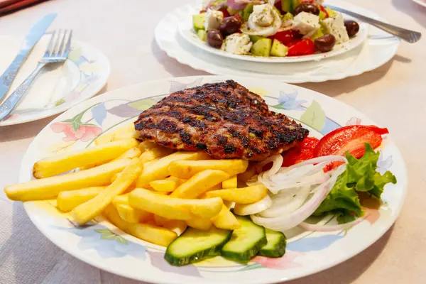 Grilled minced beef patty served with french fries and fresh vegetables on a table