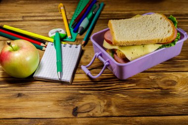 Okul konseptine geri dönelim. Okul gereçleri, elma ve beslenme çantası ve ahşap bir masada sandviçler.
