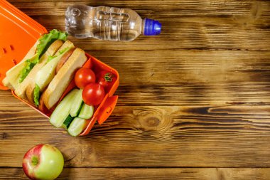 Bir şişe su, elma ve beslenme çantasıyla birlikte sandviçler ve taze sebzeler. Üst görünüm, alanı kopyala