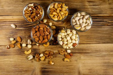Ahşap masada fındık çeşitleri. Badem, fındık, şam fıstığı, ceviz ve cam kaselerde ceviz. Üst Manzara. Sağlıklı yeme kavramı