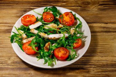 Lezzetli tavuk göğsü salatası, taze roka ve ahşap masada kiraz domatesleri.