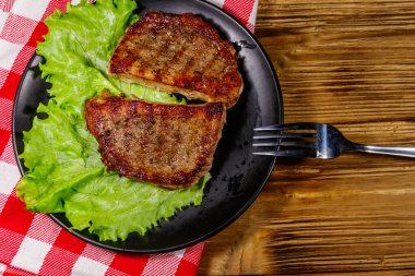 Ahşap masada marul yapraklı ızgara domuz bifteği. Üst görünüm