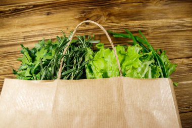 Yeşil soğanlı kağıt torbası, biberiye, marul yaprakları ve ahşap masada maydanoz. Üst Manzara. Sağlıklı gıda ve market alışverişi kavramı