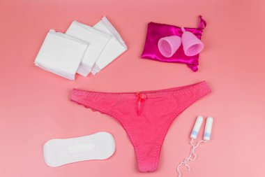 Regl bardakları, hijyenik pedleri ve pembe arka planda tamponları olan kadın külotları. Üst Manzara. Kritik günler, regl dönemi, kadın hijyeni