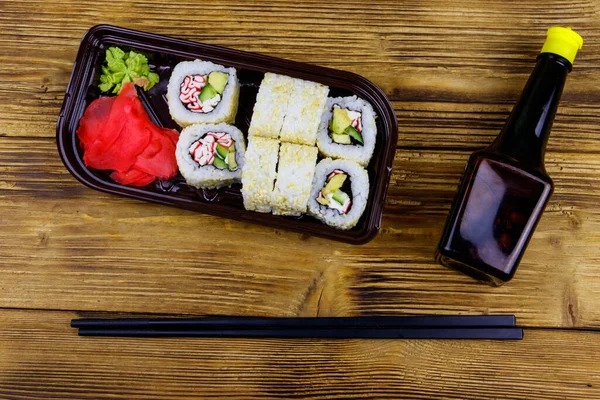 Uramaki sushi rolls with surimi in plastic box on wooden table. Top view. Sushi for take away or delivery of sushi in plastic container