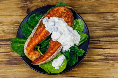 Ahşap masada ıspanaklı ve tartar soslu ızgara somon bifteği. Üst görünüm