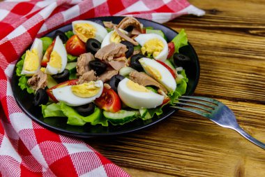 Marul, siyah zeytin, yumurta ve ahşap masada taze sebzeli lezzetli ton balığı salatası.