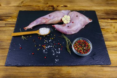 Çiğ tavşan bacağı ve siyah tahta tahta üzerinde baharatlar.