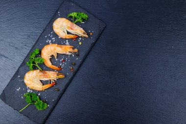 Siyah zemin üzerinde maydanozlu, tuzlu ve biberli büyük çiğ karidesler. Üst görünüm, alanı kopyala