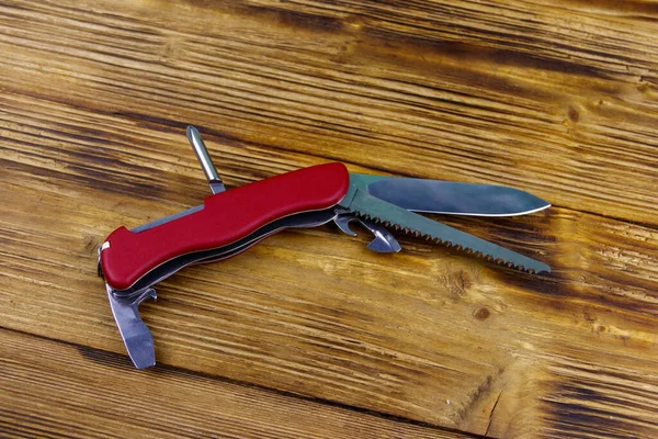Red all purpose pocket knife on a rustic wooden background. Top view