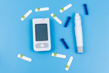 Dijital glukometre, tükenmez kalem, tek kullanımlık iğneler ve pastel mavi arka planda test şeritleri. Üst Manzara. Diyabet kavramı