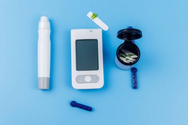Dijital glukometre, tükenmez kalem, tek kullanımlık iğneler ve pastel mavi arka planda test şeritleri. Üst Manzara. Diyabet kavramı